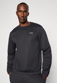 Mörkgrå sweatshirt med långa ärmar, runt halsringning, elastisk nederkant och en liten vit logotyp på bröstet. Slät, stretchig tyg.