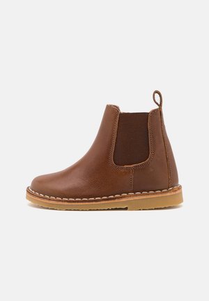 Brune lær ankelstøvle med elastisk sidepanel, rund tå, stikninger og en trækflap, hvilende på en gummisål.