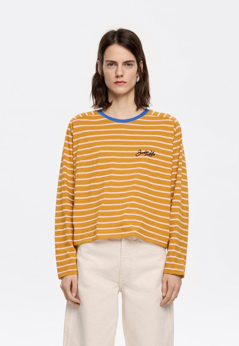 Geel en roze gestreepte shirt met lange mouwen en een blauwe kraag. Bevat een klein geborduurd tekstdetail. Gedragen met lichte broek.