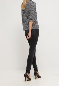 Schwarze skinny Jeans kombiniert mit einem grauen, strukturierten Strick-Oberteil mit Dreiviertelärmeln, getragen mit schwarzen High-Heels.