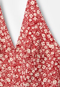 Bralette floreale rosso con scollatura a V, realizzato in tessuto morbido con un aspetto texturizzato. Motivi floreali bianchi su tutta la superficie.