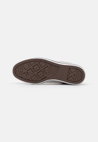 Brown rubber shoe sole with diamond-shaped tread pattern and white side trim, featuring a black logo near the heel.