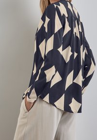 Camicia a maniche lunghe con base blu navy e motivo a rombi bianco sporco. Tessuto morbido, vestibilità ampia, con orlo arrotondato e maniche rilassate.