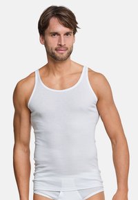 Hvid bomulds tanktop med tynde stropper, tætsiddende pasform og glat tekstur, med kontrasterende hvide syninger. Båret af en mandlig model.