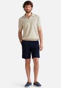 Krémové polo tričko na krátký rukáv s límečkem, spárované s námořnickými šortkami a modrými lodními botami. Neformální design s pohodlným střihem a texturovanou tkaninou.