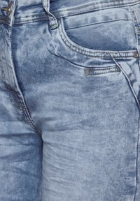 Light blue, faded denim shorts with a smooth texture, five pockets, and yellow stitching accents near the waist and pockets.