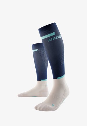 Calze a compressione con una parte superiore blu navy e accenti blu chiaro, e una sezione del piede bianca. Motivi testurizzati per traspirabilità e supporto.