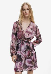 Kleid mit Blumenmuster in Rosa- und Lilatönen, mit tiefem Ausschnitt, langen Ärmeln und einem verstellbaren Bindegürtel in der Taille. Leichtes Material.
