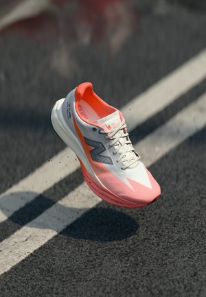 Chaussure de course avec une tige blanche et rose, présentant une texture en maille, des accents réfléchissants et une semelle rembourrée. Conception légère pour la performance.