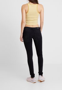 Jeans skinny negros con una cintura alta, combinados con una camiseta de tirantes corta a rayas amarillas y blancas. Los zapatos son zapatillas deportivas rosa claro con detalles grises.