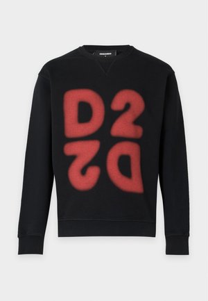 Jeune homme portant un sweat-shirt noir avec un grand graphisme rouge 2022, un short noir avec un logo blanc, des chaussettes blanches et des chaussures de sport noires, debout droit.