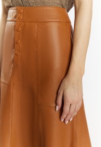 Brown leather skirt with a high waist, featuring a row of five buttons, smooth texture, and a fitted design.