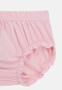 Vaaleanpunainen puuvillainen vaippakotelo, jossa on kootut joustovyötärö ja lahkeensuuhait, pehmeä kangaslaatu ja yksinkertainen muotoilu.