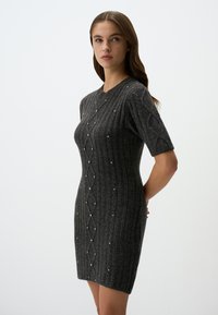 Robe en tricot charbon avec une texture côtelée et des manches courtes, mettant en valeur un motif diamant rehaussé de petits accents argentés.