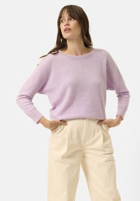 Pull en tricot lilas avec un col rond et des manches longues, associé à un pantalon taille haute de couleur crème avec des poches.