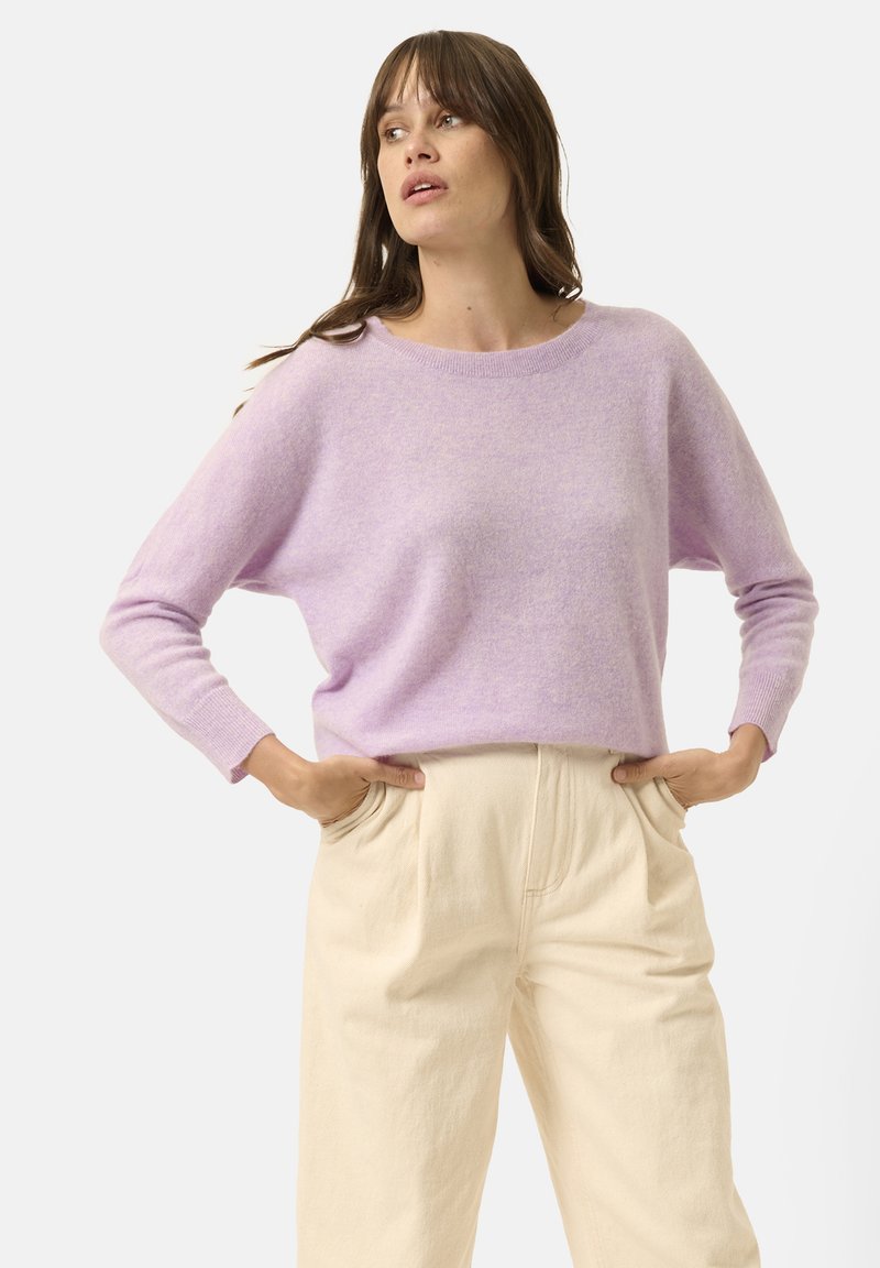Pull en tricot lilas avec un col rond et des manches longues, associé à un pantalon taille haute de couleur crème avec des poches.