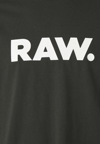 Sort bomulds T-shirt med fed hvid tekst, der står "RAW." i et rent, moderne skrifttype. Blød tekstur med en afslappet pasform.