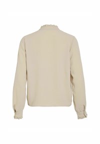 Långärmad beige blus med en texturerad yta, volangkrage och elastiska manschetter. Rakt skuren med en enkel, ren design.