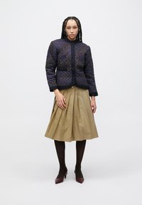 Casaco acolchoado azul-marinho com gola redonda e fecho de botões frontal, combinado com uma saia plissada bege e collants escuros.