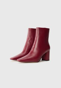 Stivali alla caviglia in pelle bordeaux con punta affusolata e tacco quadrato spesso. Texture liscia e design elegante, adatti per vari outfit.