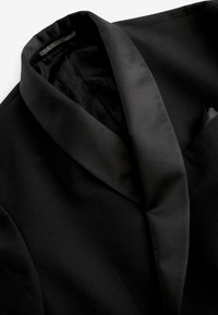 Černý blazer s saténovým šálovým límcem, hladkou texturou látky a malým kapsičkovým detailem na přední levé straně.