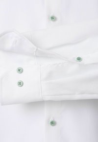 Weißes Hemd mit hellgrünen Knöpfen, das einen gefalteten Ärmel und einen geknöpften Manschette zeigt.