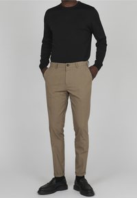 Svart långärmad skjorta i kombination med beige skräddarsydda byxor. Byxorna har en slät textur, knäppning med knapp och fickor. Svarta skor fulländar looken.