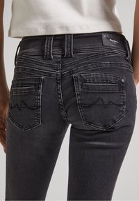 Černé džíny z denimu se slim fit designem, které mají dvě zadní kapsy s vlnitým švem a roztrhanými okraji na kapsách.