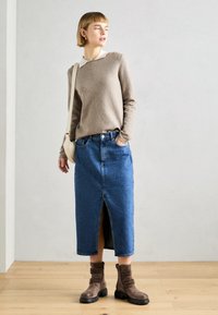 Beige pletený svetr, modrá denimová sukně střední délky s předním rozparkem a hnědé kotníkové boty. Přirozená textura a volný střih.