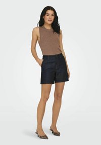 Brązowy żeberkowany top na ramiączkach w połączeniu z ciemnymi dżinsowymi szortami. Modelka nosi baleriny w gepardzim wzorze. Szorty charakteryzują się klasycznym krojem i przednimi kieszeniami.