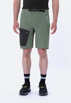 Green athletic shorts with a black pocket, adjustable belt, zippered side pockets, and a smooth texture. Worn with black socks and shoes.