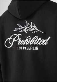 Sudadera negra con texto blanco "Prohibido" y "10119 BERLÍN" con un diseño de hoja encima de las letras. Fabricada en un tejido suave, estilo con capucha.