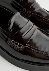 Mocassins en cuir bordeaux foncé brillants au design classique, avec une bande sur le dessus, des coutures détaillées et des semelles en caoutchouc.