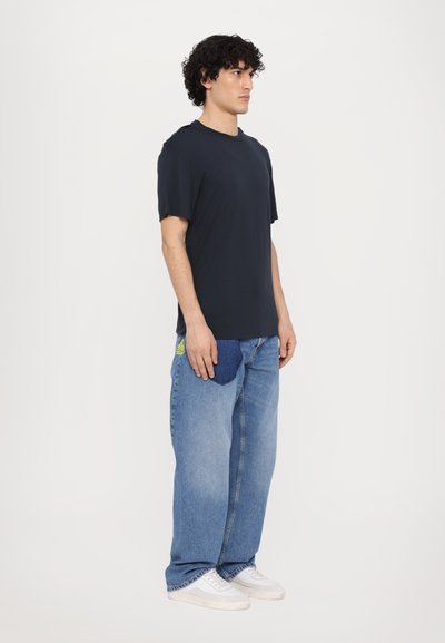 T-shirt navy à manches courtes associé à un jean léger oversize bleu clair avec une poche en patch unique en denim contrasté. Baskets blanches.
