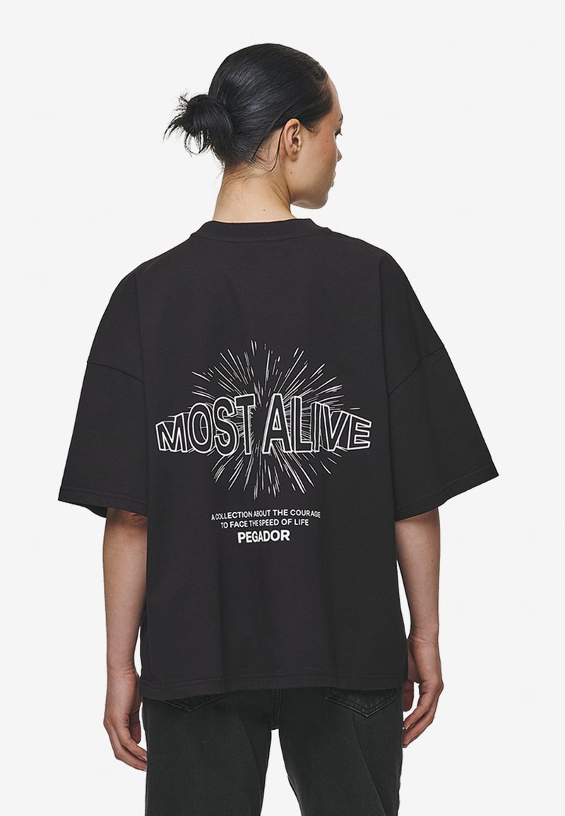 Zwarte oversized t-shirt met een ronde hals en korte mouwen. Kenmerkt zich door de witte opdruk "MOST ALIVE" en een explosie-ontwerp op de achterkant.