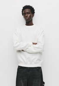 Hvid crewneck sweatshirt med lange ærmer, lavet af blødt stof, parret med mørk denim jeans med sidelomme-detalje.