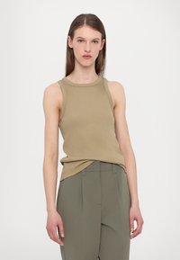 Khaki sleeveless top with ribbed texture, round neckline, and fitted cut, paired with high-waisted, loose olive green trousers.