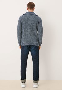 Stickad tröja i marinblått med en texturerad yta och bred krage, kombinerad med mörk denim jeans och vita sneakers med grå detaljer.