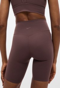 Καφέ ποδηλατικά σορτς με ψηλή μέση και λεία υφή, με διακριτικό λογότυπο Nike στο πίσω μέρος και εφαρμοστή σχεδίαση που φτάνει μέχρι το μέσο του μηρού.