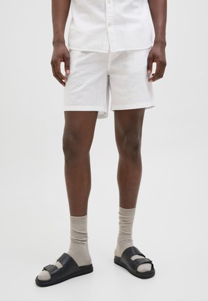 Shorts en lin blancs à coupe droite, associés à des sandales noires et des chaussettes beiges. Texture lisse, design minimal, et sans motifs visibles.