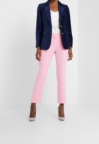 Marinblå strukturerad blazer med två guldknappar, kombinerad med slimmade rosa byxor. Modellen bär beige stilettklackar. Släta, skräddarsydda tyger.