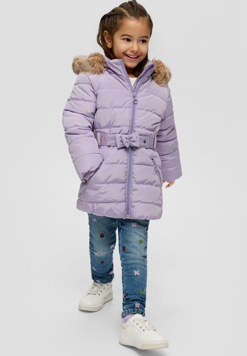 Jasnofioletowa kurtka puchowa z kapturem z sztucznego futra, paskiem w talii i zamkiem błyskawicznym z przodu. Połączona z dżinsami z haftem i białymi sneakersami.