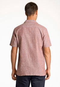 Camisa de manga corta en un tejido texturizado de color rojo claro con un patrón sutil; presenta un cuello clásico y un dobladillo recto.