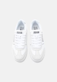 Άσπρα αθλητικά παπούτσια με λείο δερμάτινο επάνω μέρος και σουέντ λεπτομέρειες. Διαθέτουν αντίθετο μαύρο κείμενο και κορδόνια. Στρογγυλερή μύτη και υφή στη σόλα.