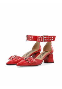 Zapatos de charol rojo con tacón bloque y punta afilada, correa de tobillo con ojales y detalle de hebilla. En el interior tienen el logo de la marca.