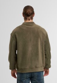 Oliwkowy polarowy sweter o luźnym kroju, z opuszczonymi ramionami i ściągaczami. Gładka tekstura, bez widocznych wzorów ani akcentów.