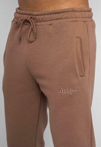 Brune bomulds-svedbukser med elastisk livrem, snor og sidelommer. Har "Dropsize" broderet i lysebrun.