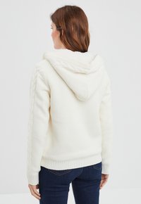 Felpa bianca con cappuccio, in tessuto strutturato, con dettagli a trecce sulle maniche e polsini e orlo a costine. La vista posteriore mostra i dettagli del design.