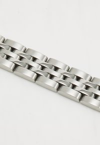 Armband aus Edelstahl mit einem glatten, abgerundeten Design, interlocking flachen Gliedern, matten und polierten Oberflächen in silberner Farbe.
