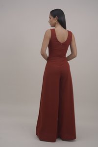 Rode mouwloze jumpsuit met een V-back ontwerp, wijde pijpen en een verborgen ritsdetail aan de achterkant. Soepele stoftextuur.